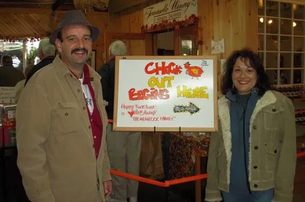 A man and woman smiling next to a white sign that reads 