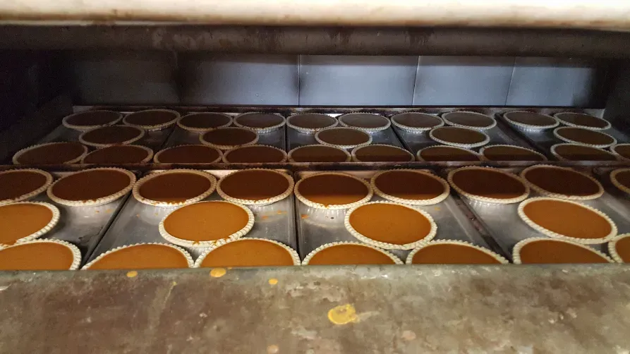 Numerous pumpkin pies baking on metal trays inside a large commercial oven.
