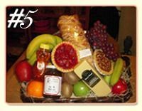 A wicker basket filled with assorted fruit, honey, jam, a loaf of bread, two small pies, and a block of cheese.