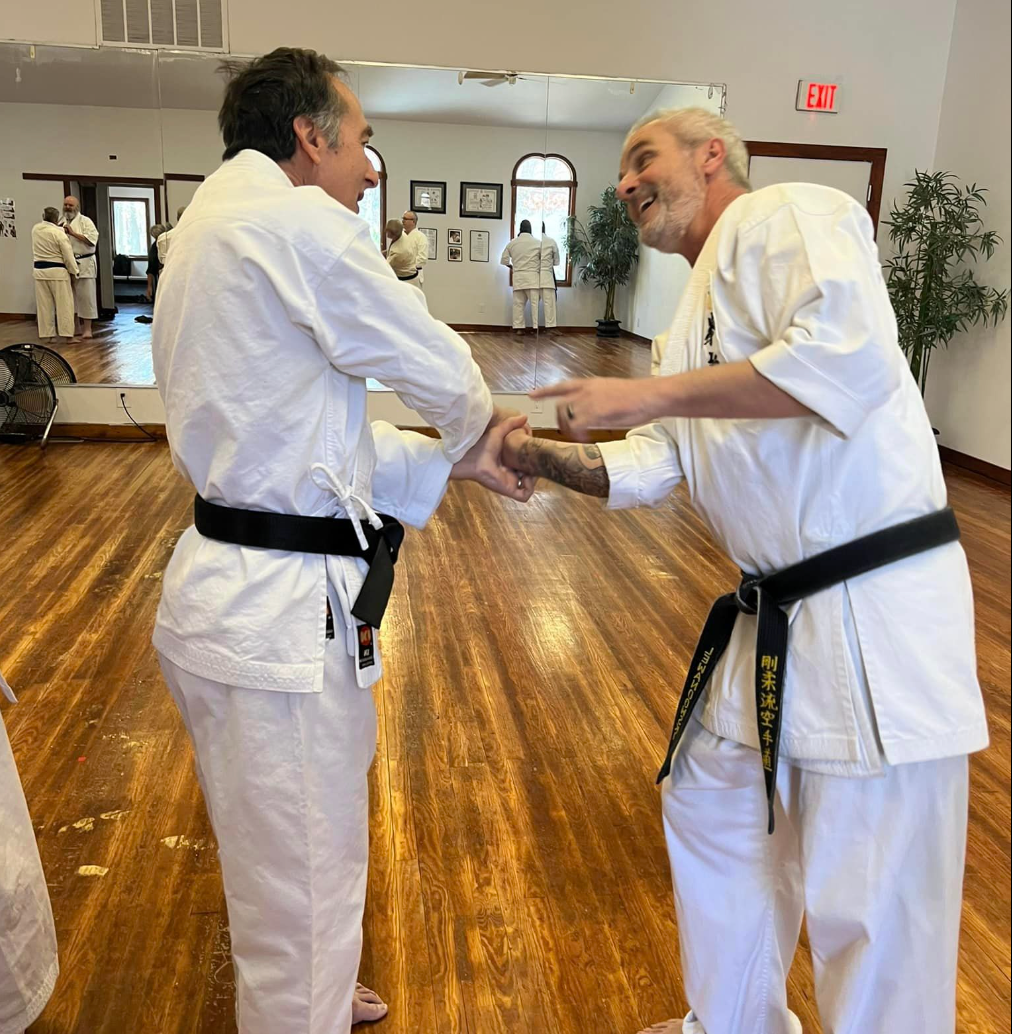 Two men in white karate uniforms are shaking hands