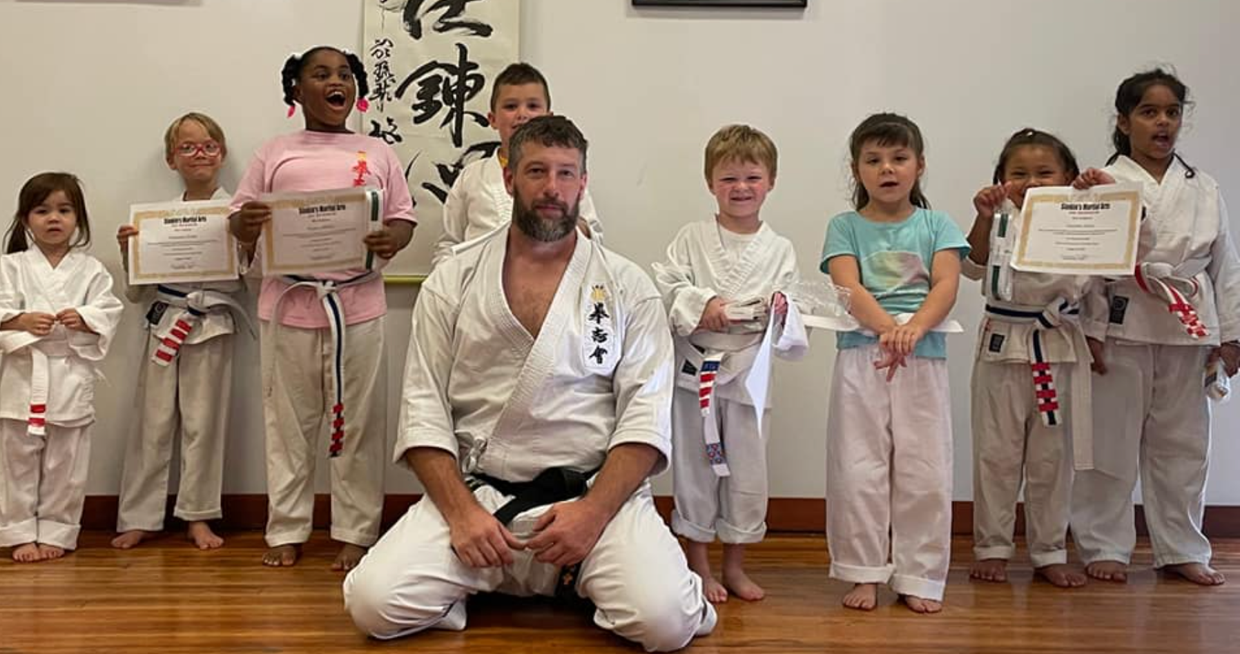 A man is kneeling down in front of a group of children holding certificates.