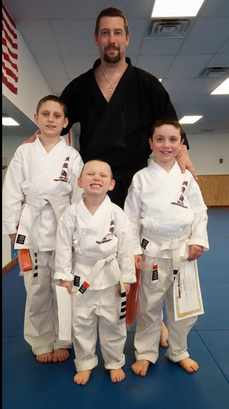 A man is standing next to three young boys in karate uniforms