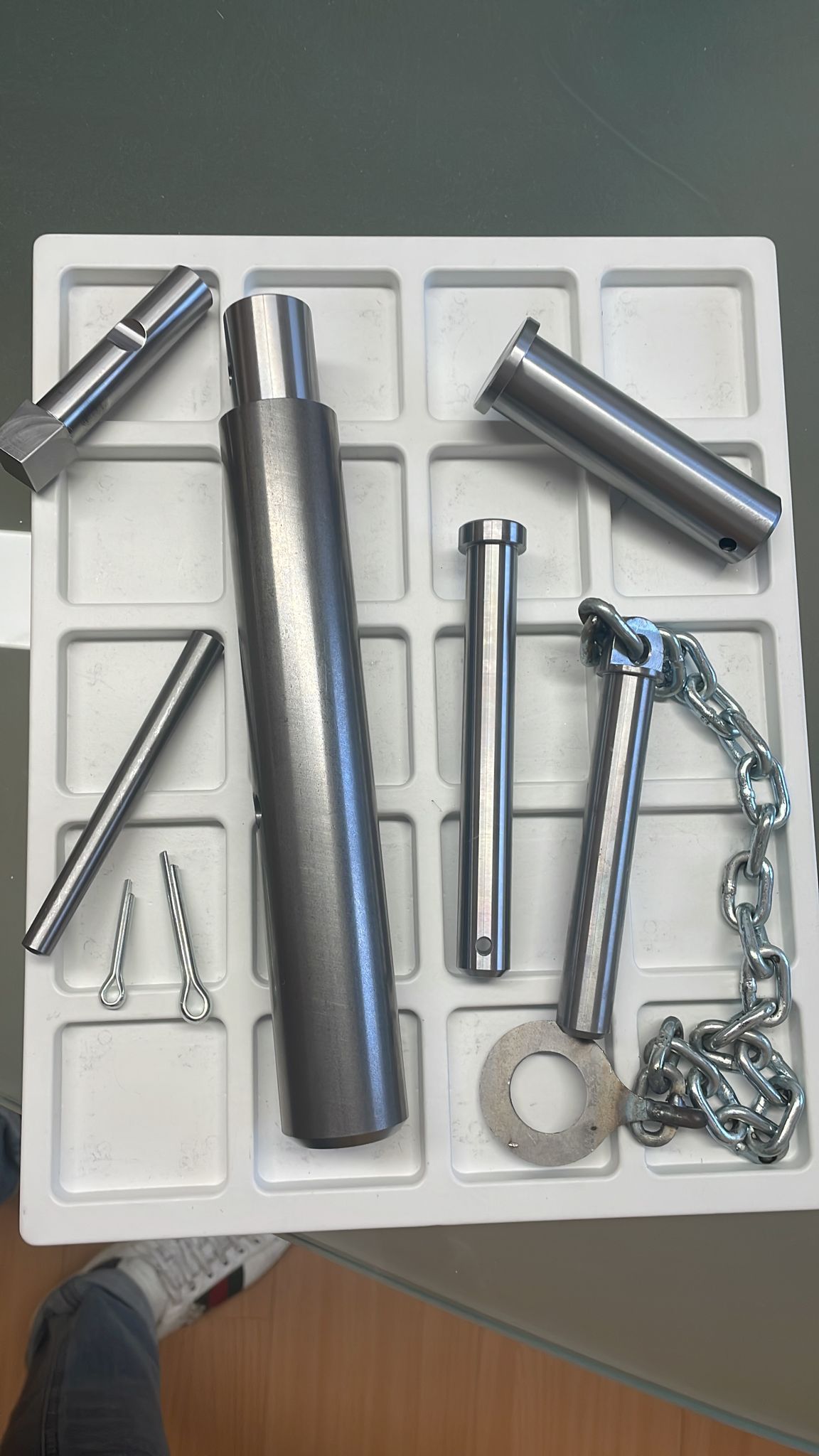 Un vassoio di plastica bianca contenente vari componenti meccanici in metallo color argento e una catena corta.