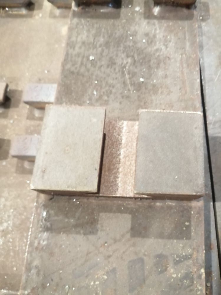 Due blocchi metallici paralleli poggiano su una superficie metallica ruvida, separati da uno stretto canale incassato di colore scuro.