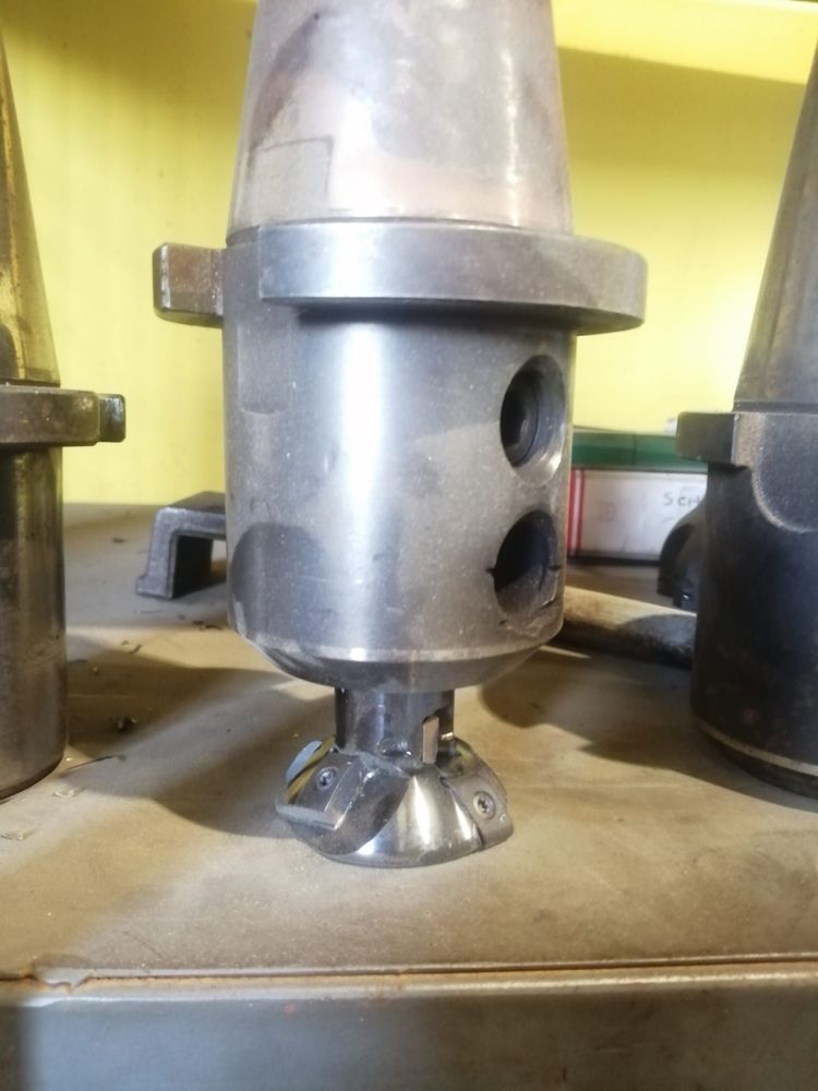 Un supporto per macchina utensile CNC di colore argento con una piccola fresa a inserti multipli nella parte inferiore, appoggiato su un banco da officina.