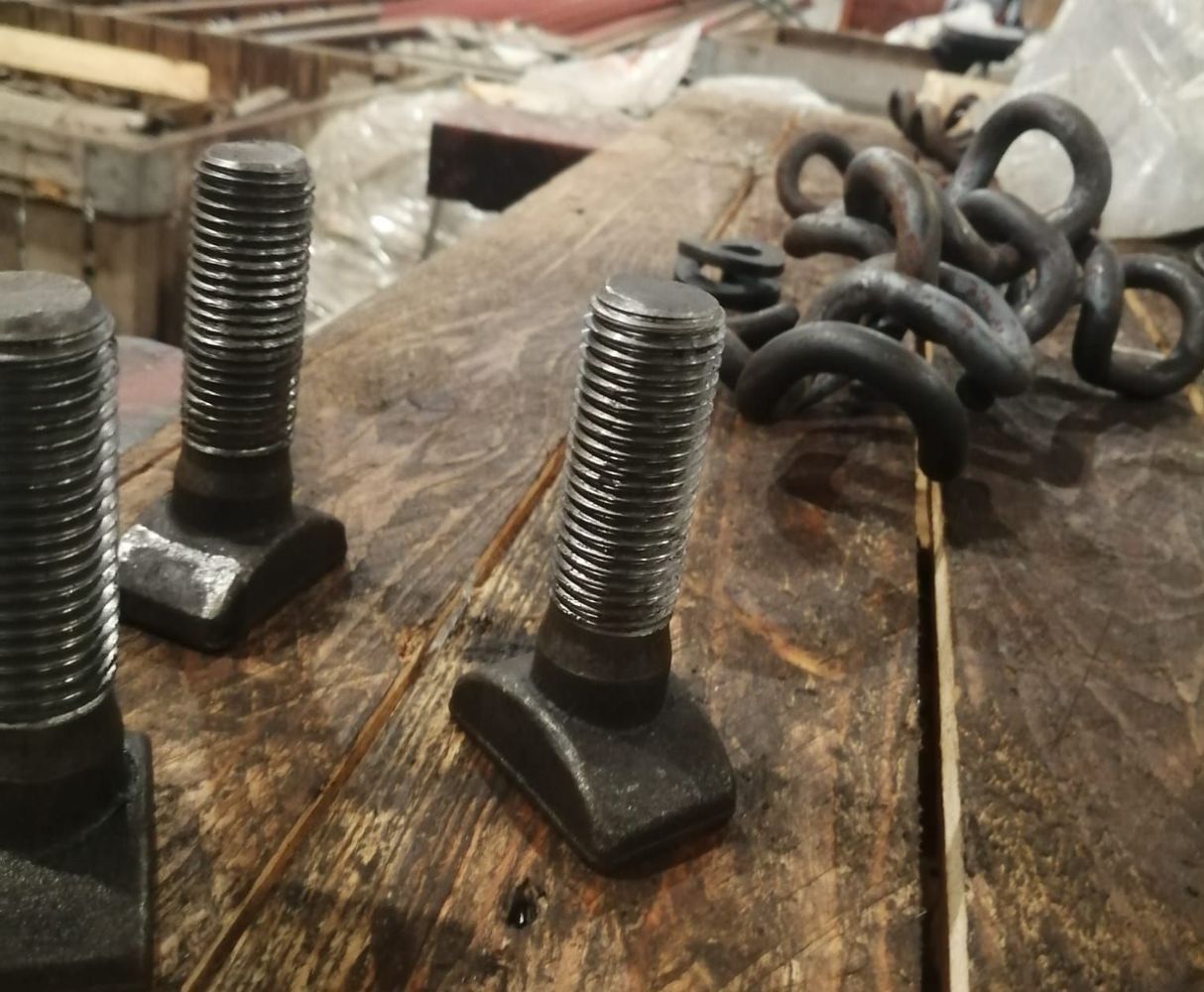 Diversi bulloni a T in metallo e spire metalliche aggrovigliate, disposti su una superficie di legno consumata dal tempo.