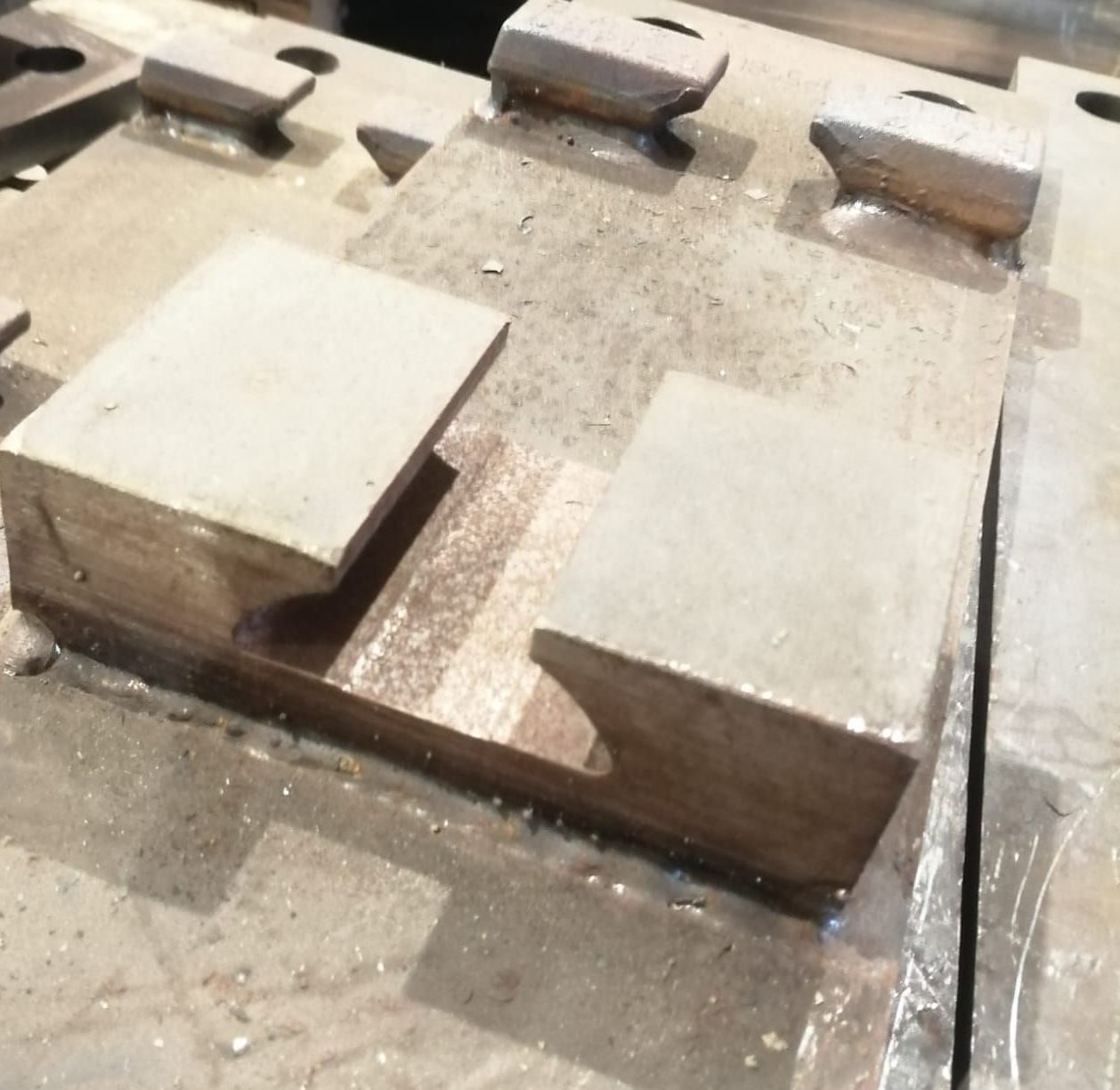 Primo piano di componenti metallici industriali con una caratteristica scanalatura a coda di rondine a forma di T saldata su una piastra piatta di acciaio grigio.