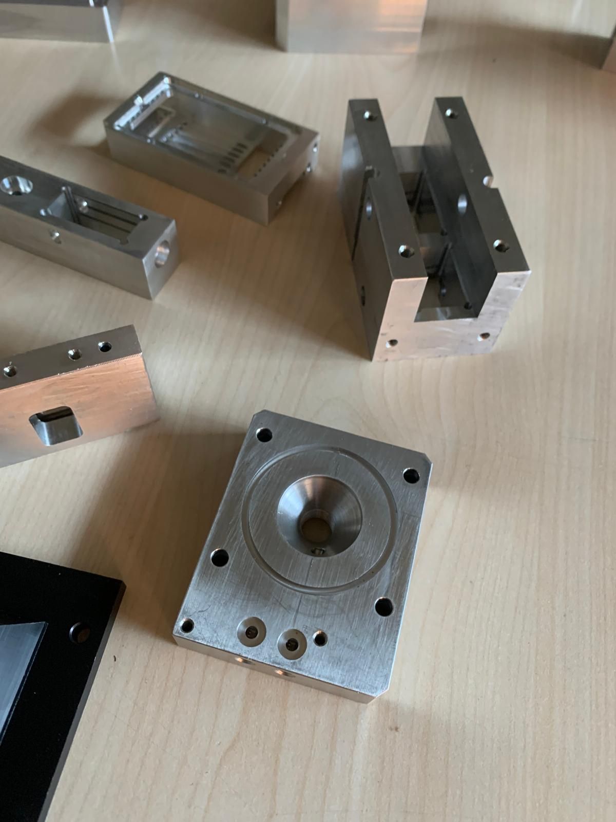 Su un tavolo di legno chiaro sono disposti diversi componenti in alluminio lavorato.