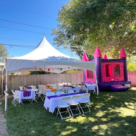 Outdoor party scene: tent, tables with purple runners, inflatable castle, backyard setting.