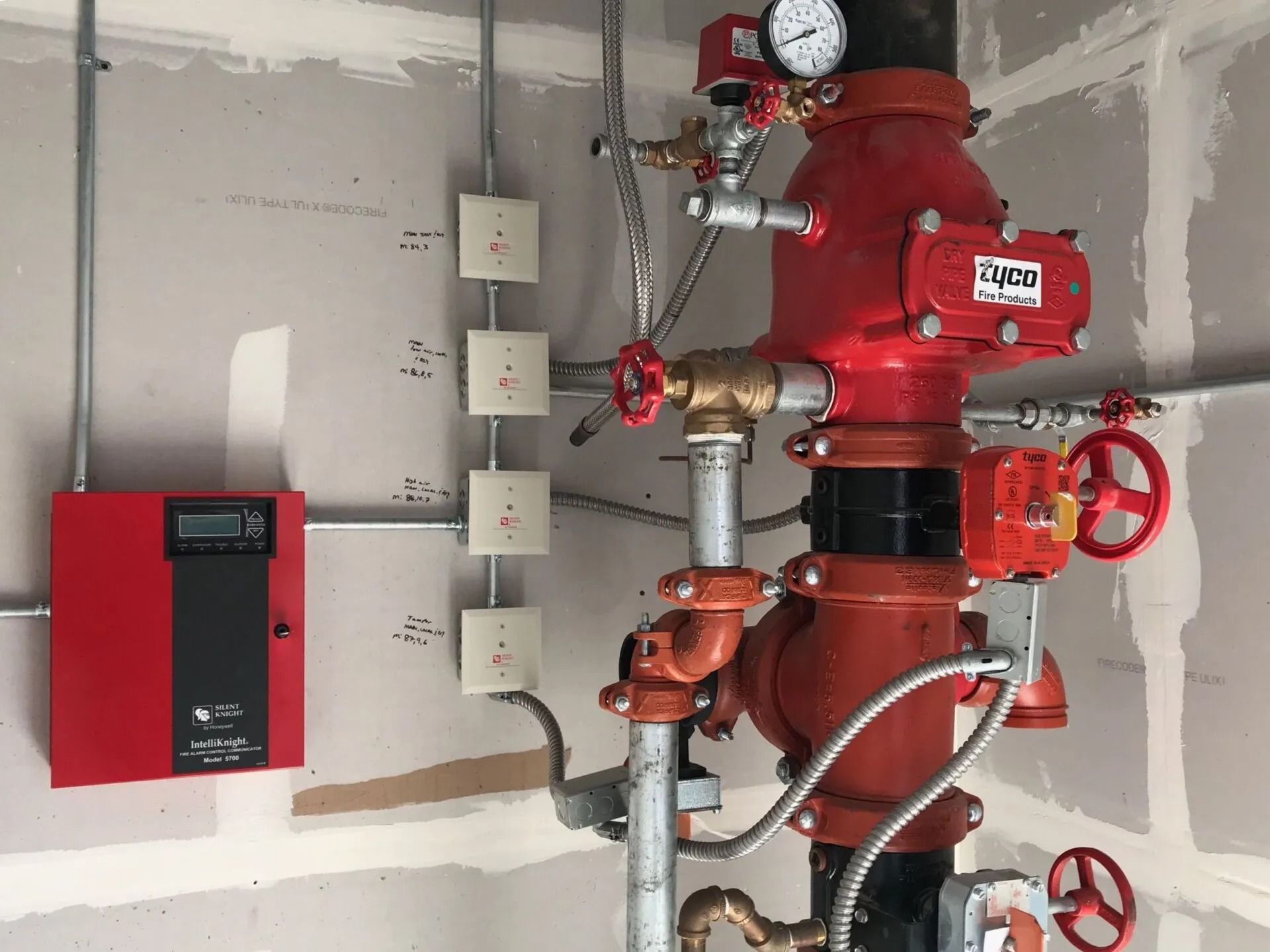 Sistema de rociadores contra incendios de color rojo con medidores, válvulas y panel de control en una pared.