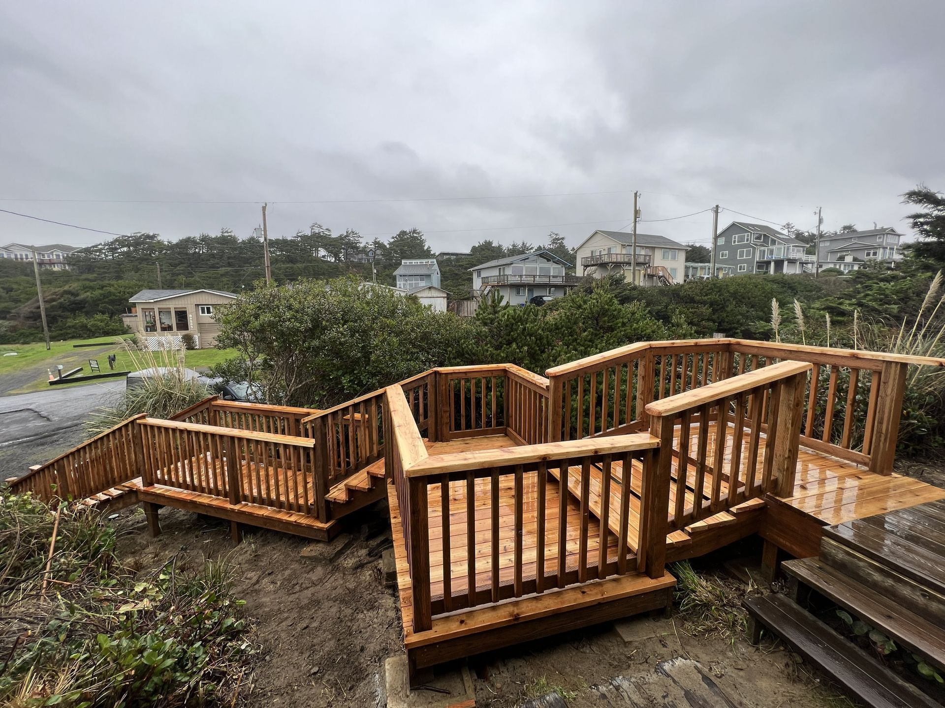 Wooden deck and stairs on a hillside overlooking houses and cloudy sky.