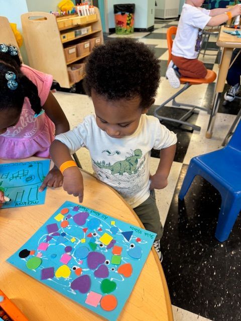 A boy and a girl are sitting at a table playing with stickers