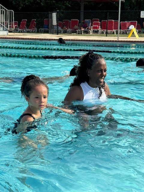 A woman is teaching a little girl how to swim in a swimming pool.