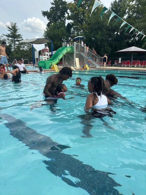 A group of people are swimming in a pool with a slide in the background