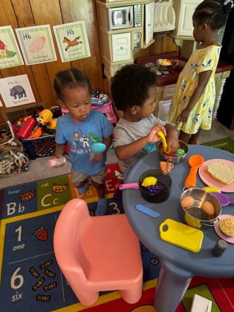 Three children are playing with toys at a table with the letters bb and cc on the rug