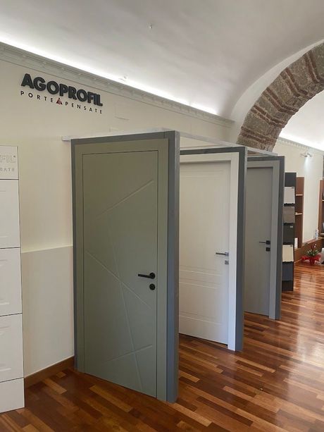 Showroom interno con diverse porte grigie e bianche in mostra sotto un soffitto a volta.