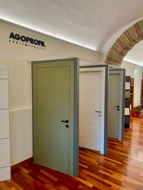 Showroom interno con diverse porte grigie e bianche in mostra sotto un soffitto a volta.