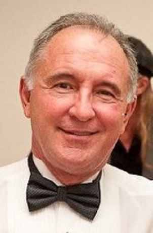 A person in a white dress shirt and a dark, textured bow tie smiling at the camera.