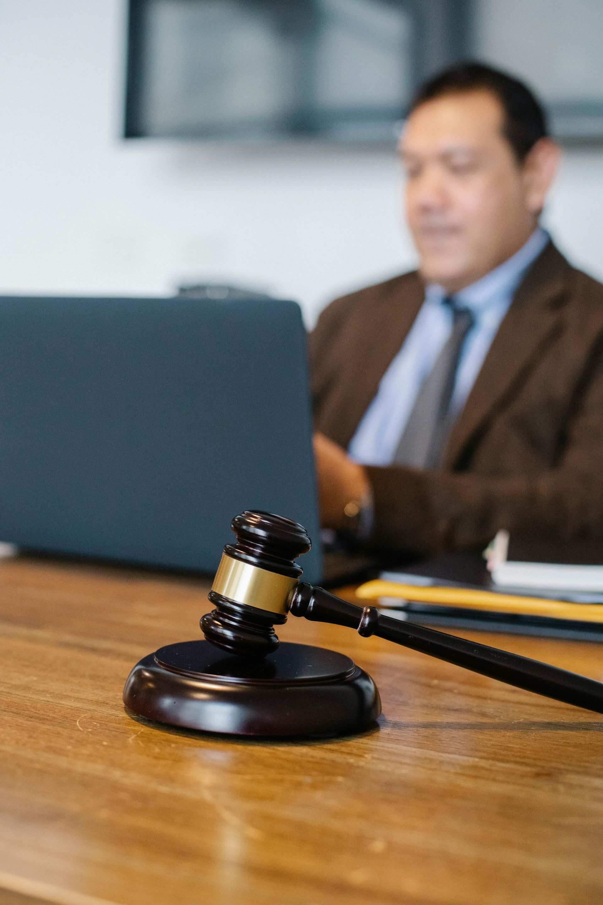 Gavel on a wooden desk with a blurred lawyer seated in the background in an office setting