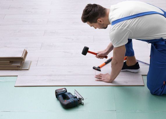 A man is hammering a nail into a wooden floor.