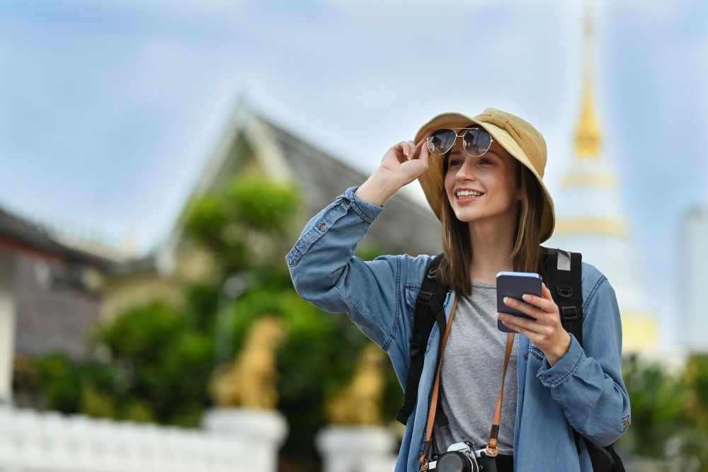 A woman wearing a hat and sunglasses is holding a cell phone.