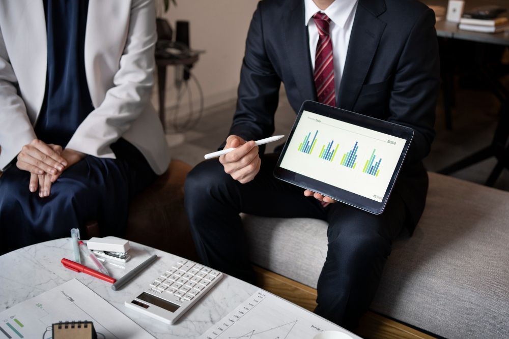 A man and a woman are sitting at a table looking at a tablet.