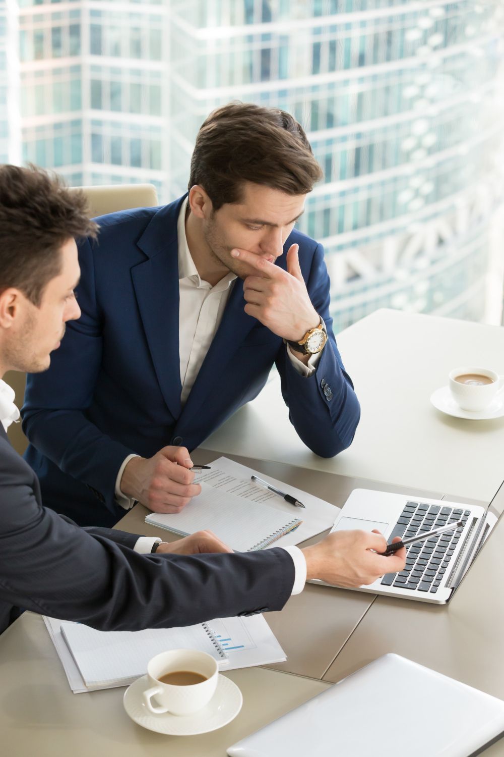 Two men are sitting at a table looking at a laptop.