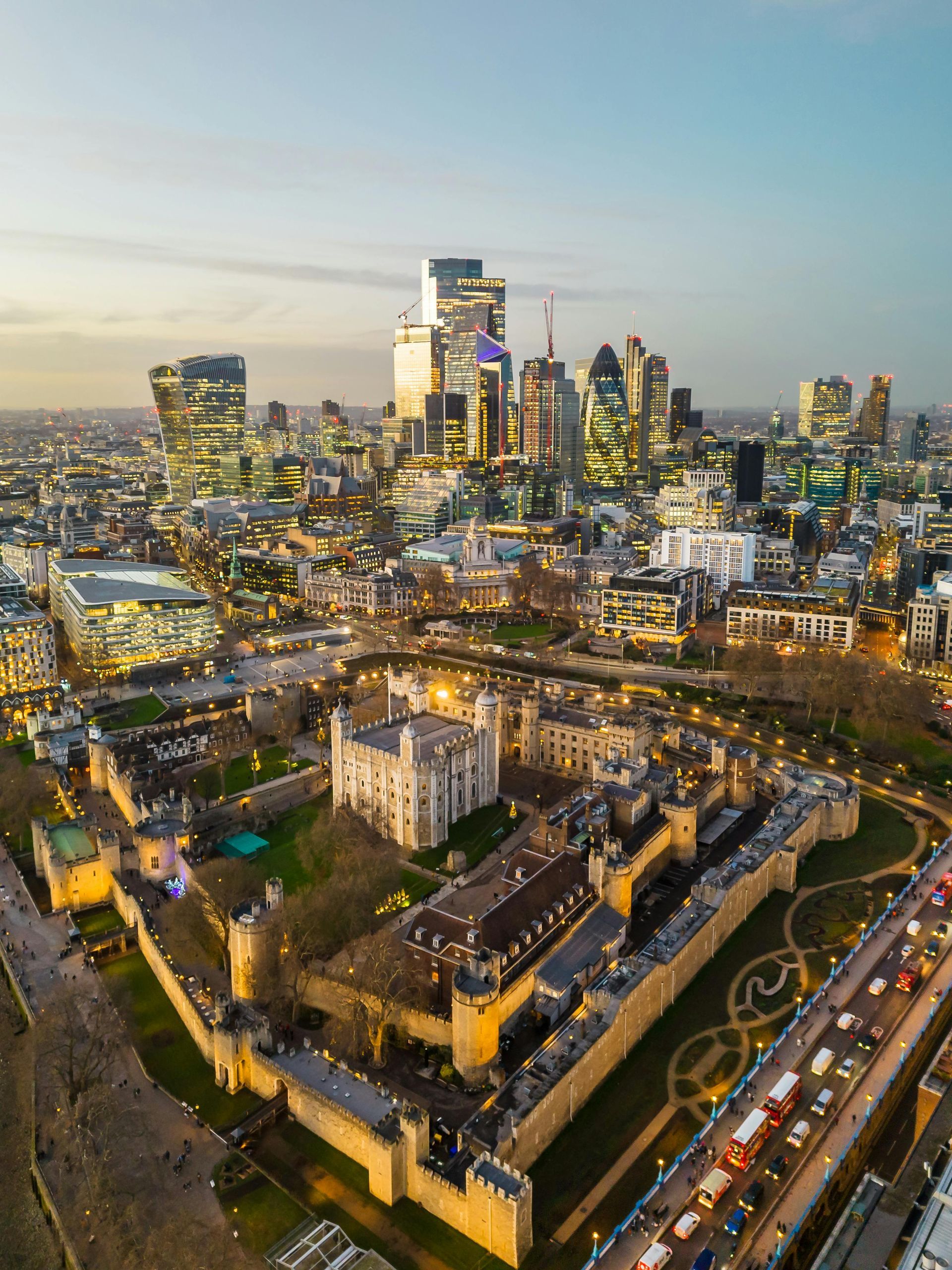 An aerial view of the tower of london at night with a city skyline in the background.