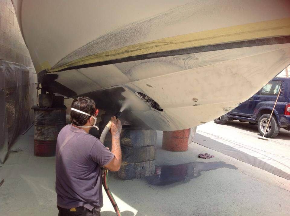 A man is sandblasting the bottom of a boat.