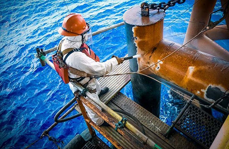 A man in a protective suit is cleaning a pipe in the ocean.
