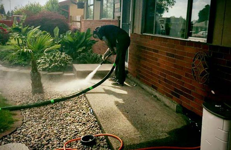 A man is cleaning a sidewalk with a hose in front of a brick building.