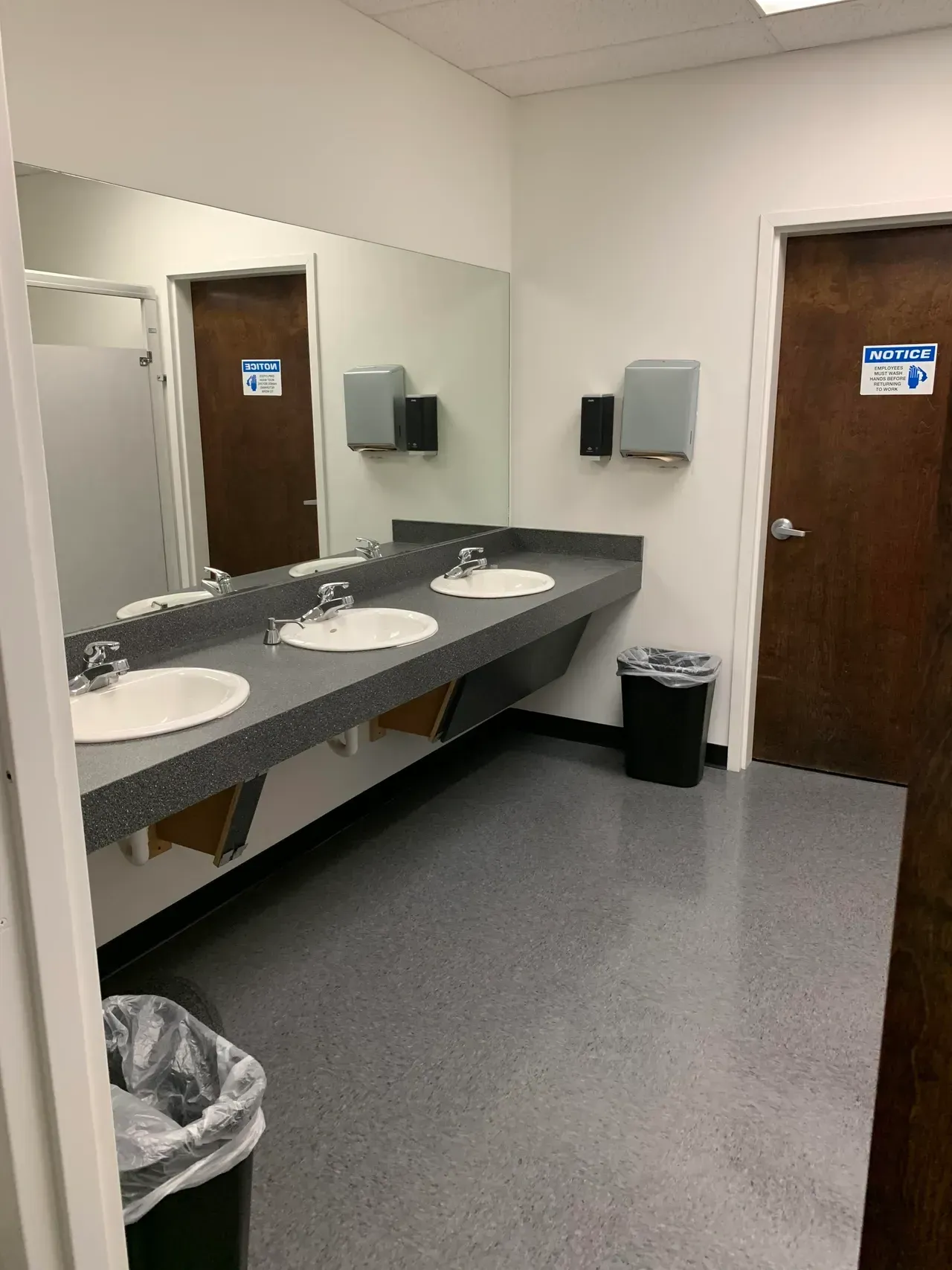 A bathroom with three sinks , a trash can , and a mirror.