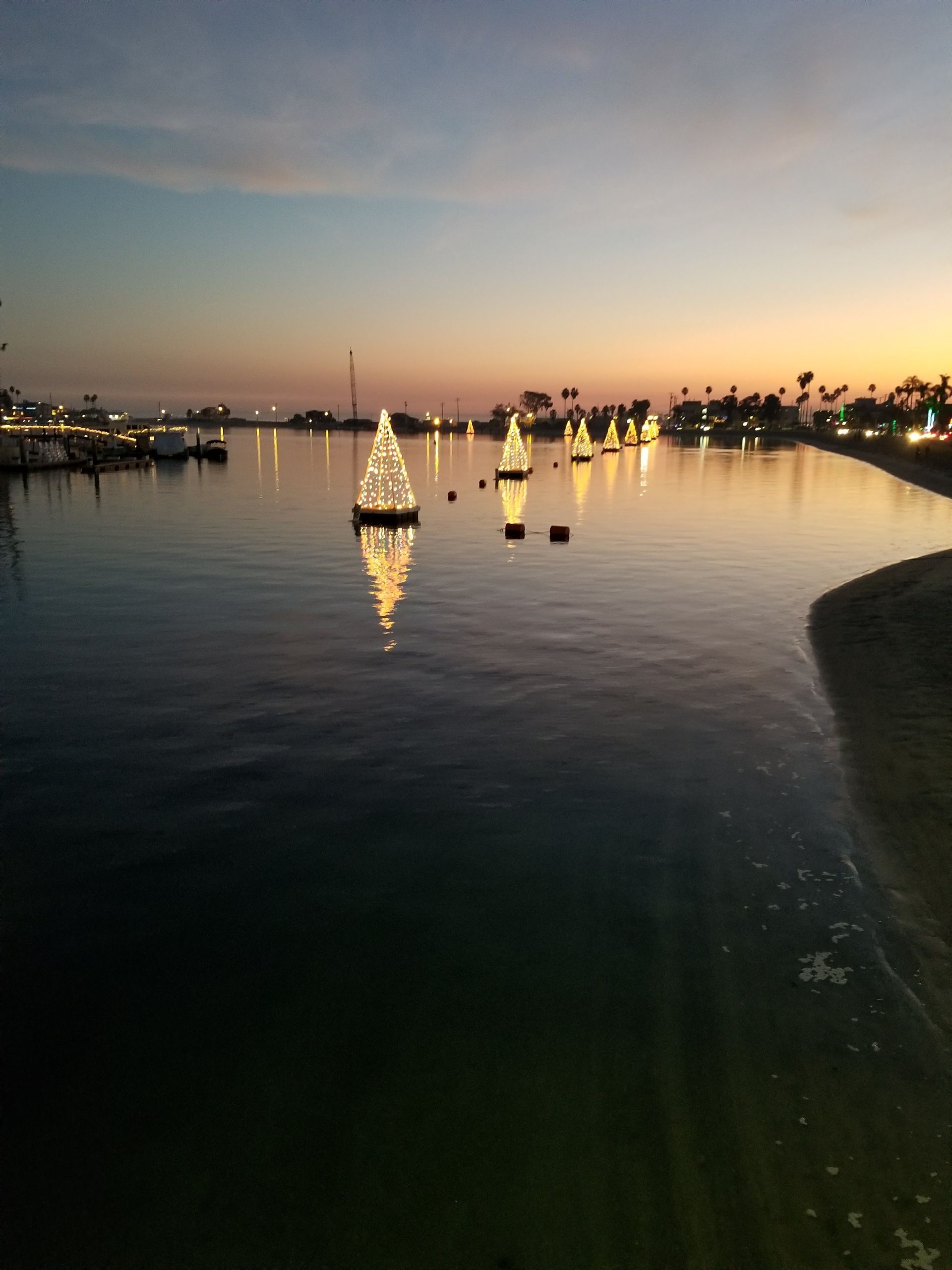 Christmas tree lights on the water at dusk. Bay with calm water reflecting lights and sky.