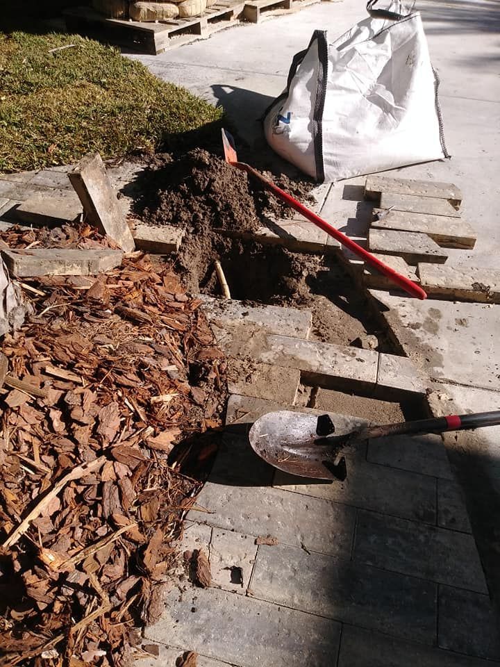 Construction site with shovels, a large bag, and exposed ground on a stone walkway.