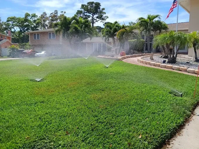 Lawn sprinklers watering a vibrant green lawn in front of a house on a sunny day.