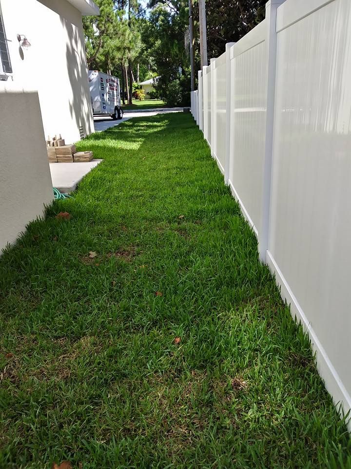 Narrow strip of green grass between a white fence and a building.