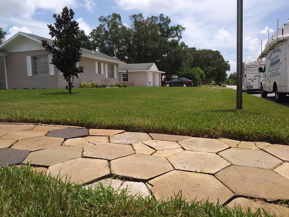Paved walkway leads to a house with a well-maintained lawn, a street, and utility trucks.