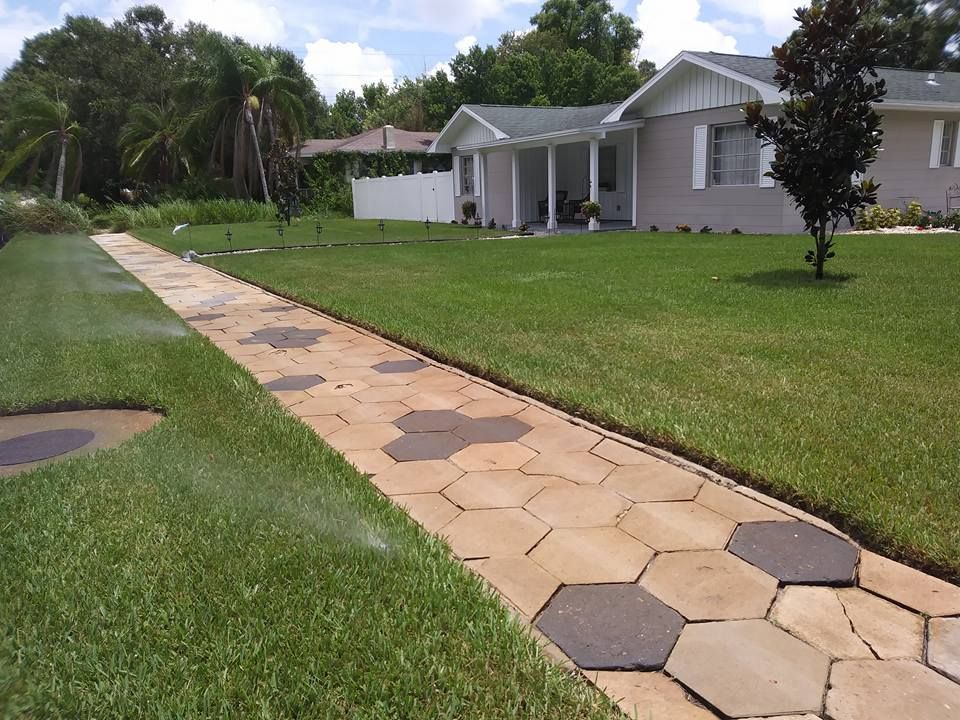 A paved walkway of hexagonal stones leads to a light-colored house with green lawn on either side.