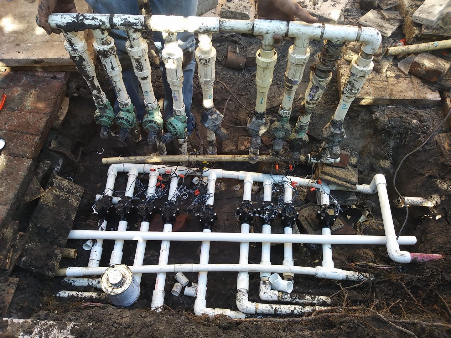 Irrigation system valves and piping, open in an excavated pit, being repaired.