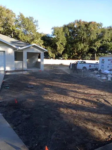 A house under construction with bare dirt in the front yard. A white truck and building materials sit nearby.