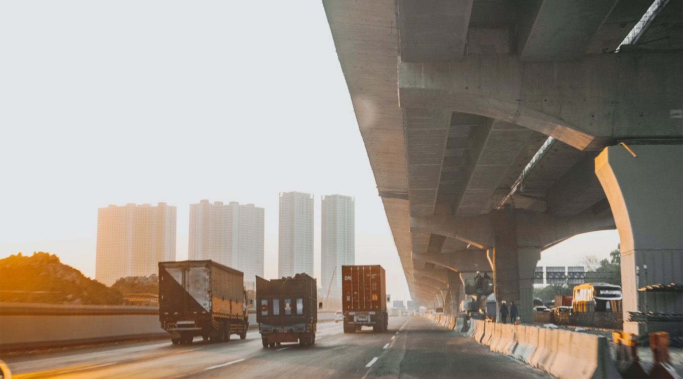 A group of trucks are driving under a bridge on a highway.