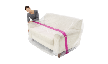 A woman is covering a white couch with plastic wrap.