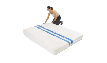 A woman is kneeling over a white mattress with blue stripes on it