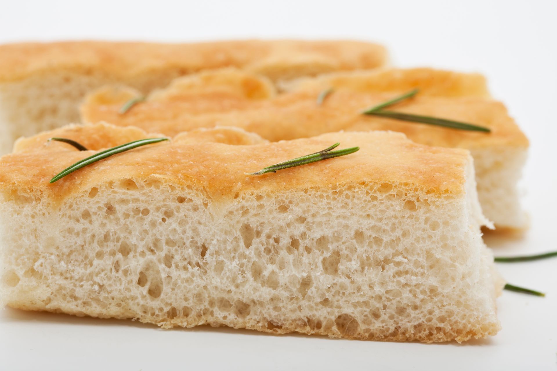 Primo piano di un pezzo di pane con rosmarino su una superficie bianca.