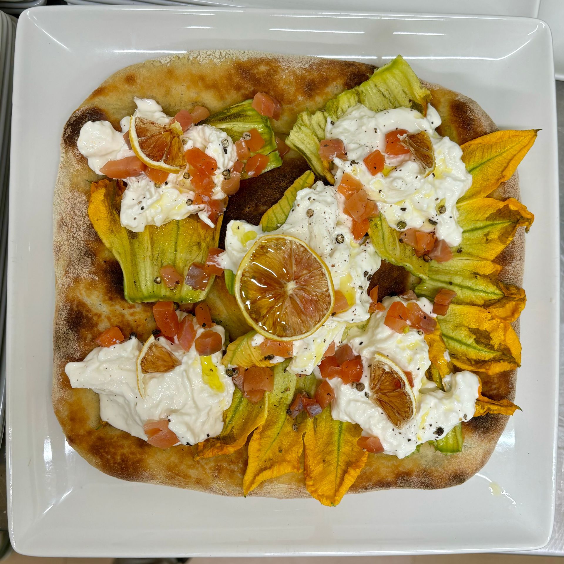 Una pizza con dei fiori sopra è su un piatto bianco.