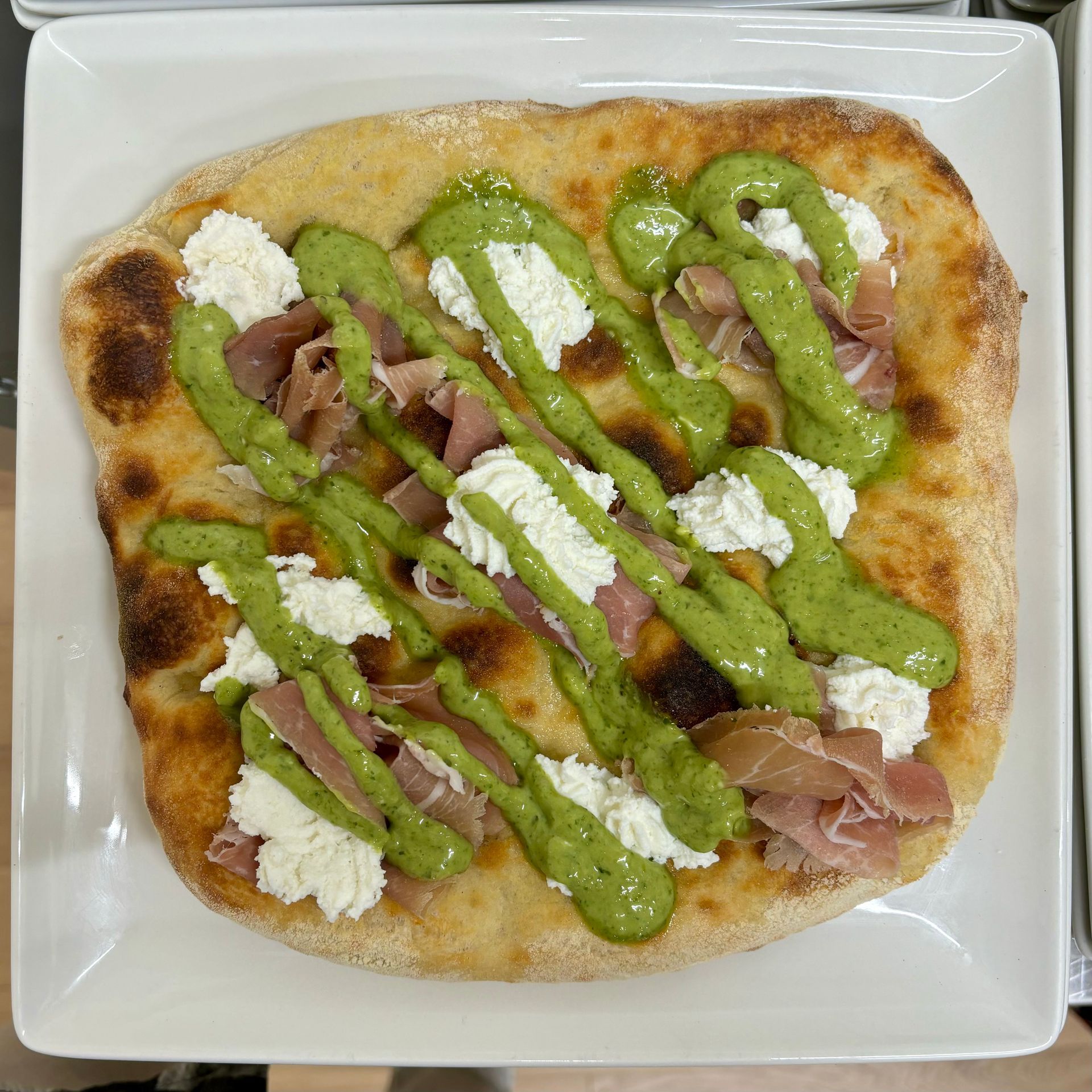 Una pizza con salsa verde e formaggio su un piatto bianco