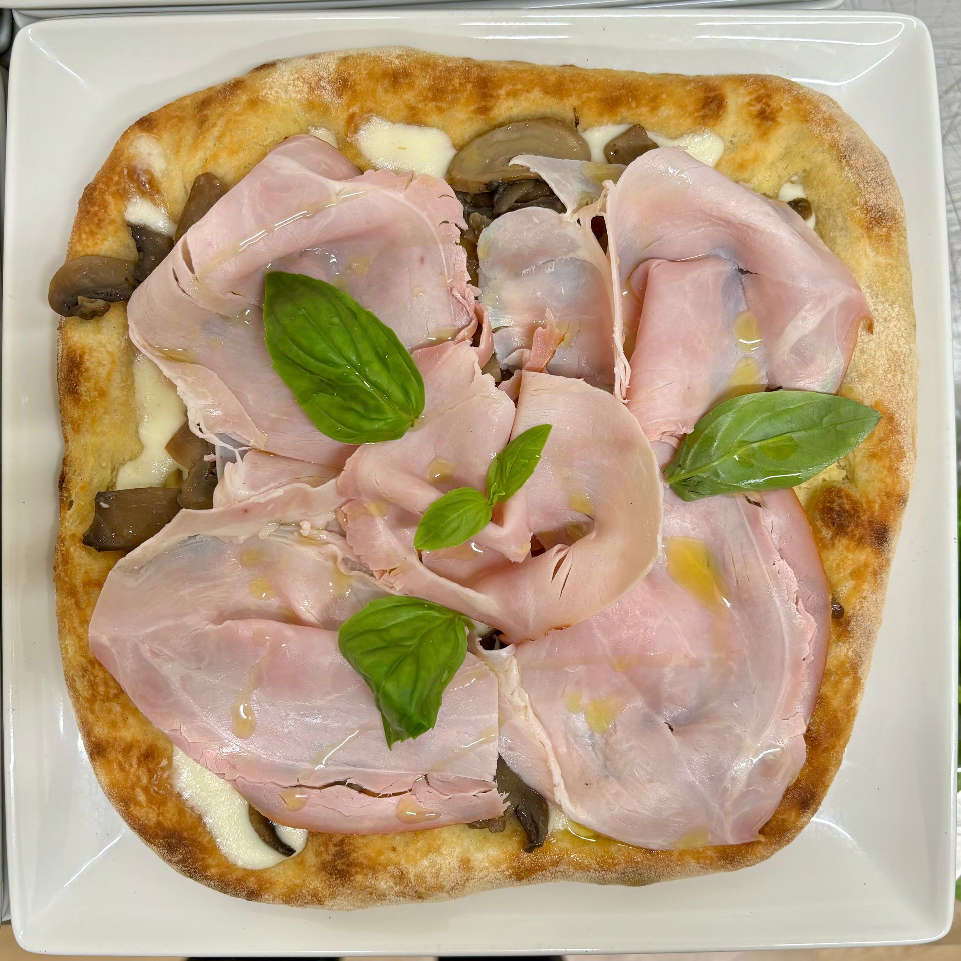 Una pizza con prosciutto, funghi e basilico su un piatto bianco