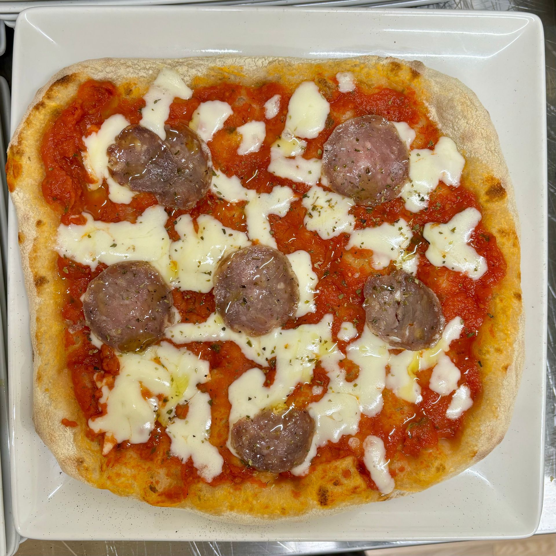 Una pizza con salsiccia e formaggio su un piatto bianco