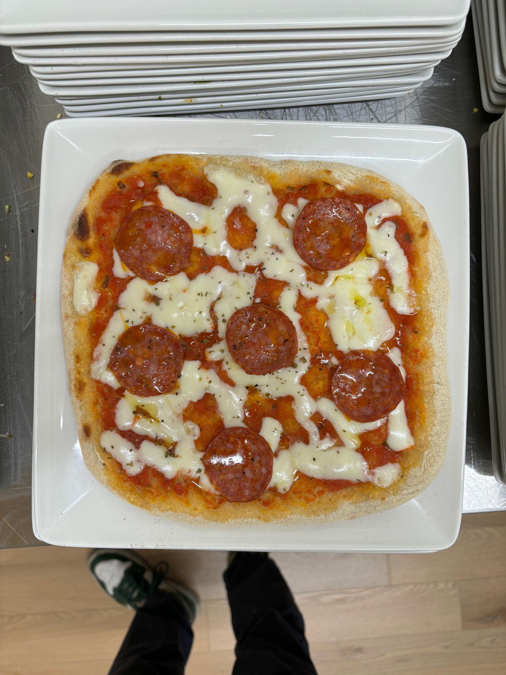 Una pizza con pepperoni e formaggio su un piatto bianco.