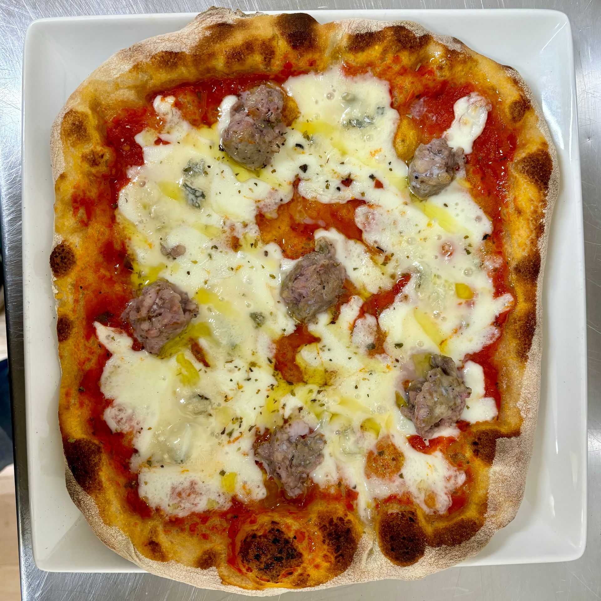 Una pizza con salsa di pomodoro, formaggio e salsiccia su un piatto bianco.